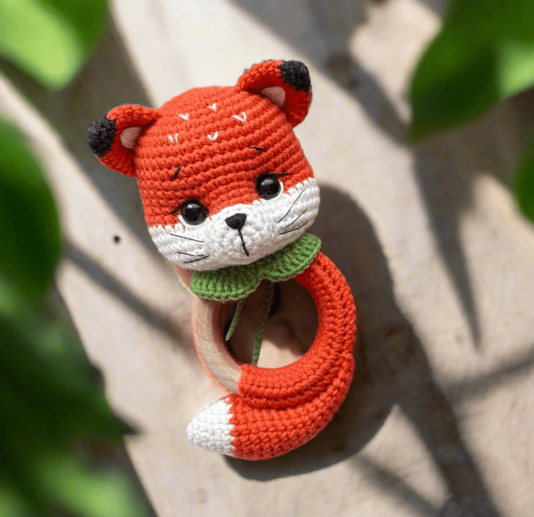 Crocheted fox-shaped baby rattle with green collar on wooden background
