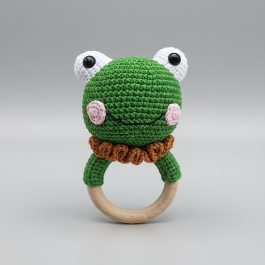 Crocheted green frog baby rattle with wooden teething ring on gray background