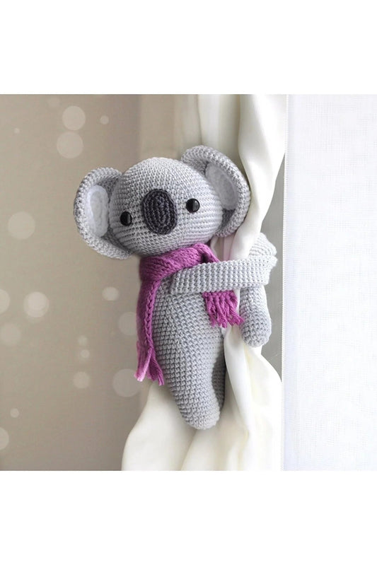 Crocheted gray elephant with pink scarf, hanging on white curtain or fabric