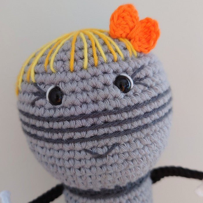 Crocheted amigurumi character with yellow hair, orange bow, and round gray body