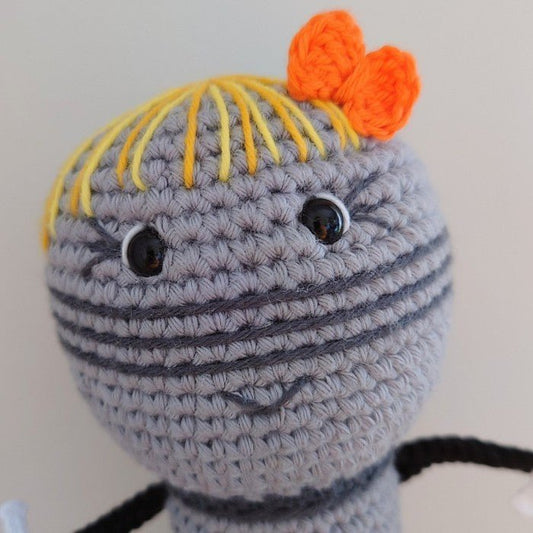 Crocheted amigurumi character with yellow hair, orange bow, and round gray body