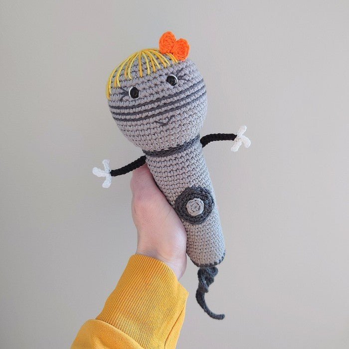 Crocheted gray robot toy with yellow hair and orange bow, held by hand