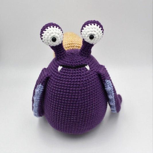 Crocheted purple monster with bulging eyes and yellow beak, plump and whimsical.