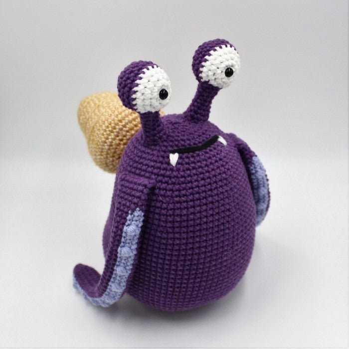 Crocheted purple snail with large white eyes and a yellow shell on gray background