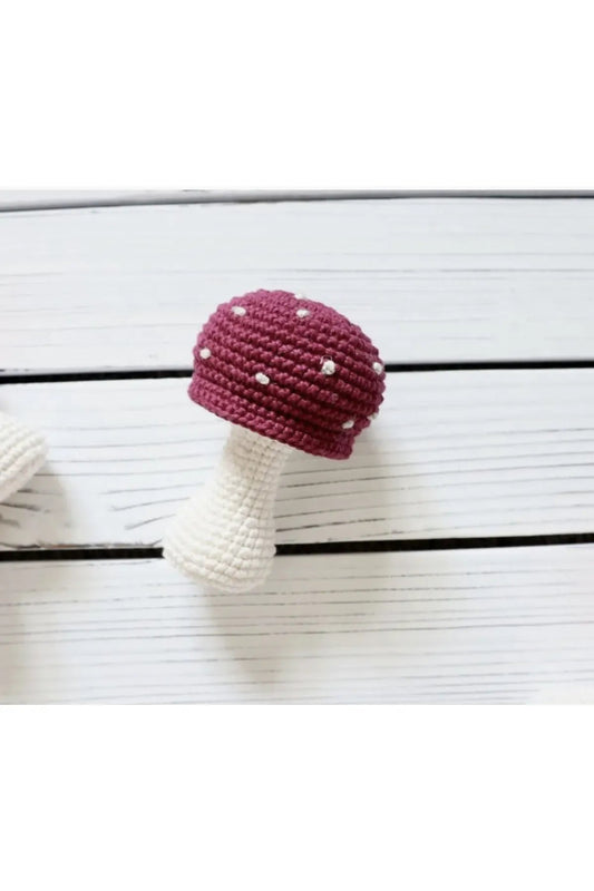 Crocheted mushroom with burgundy cap and white stem on wooden background
