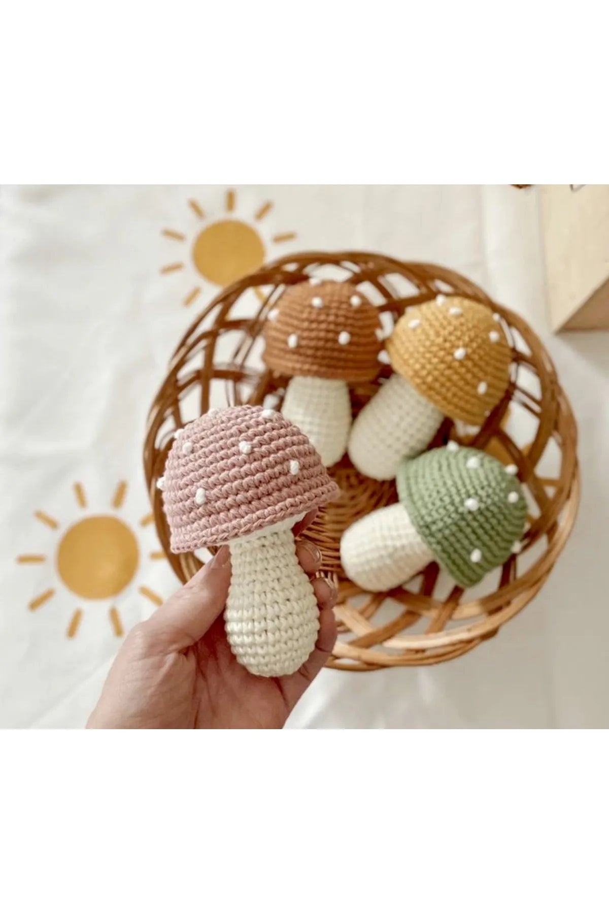 Crocheted mushrooms in pastel colors nestled in a woven basket with sun illustration