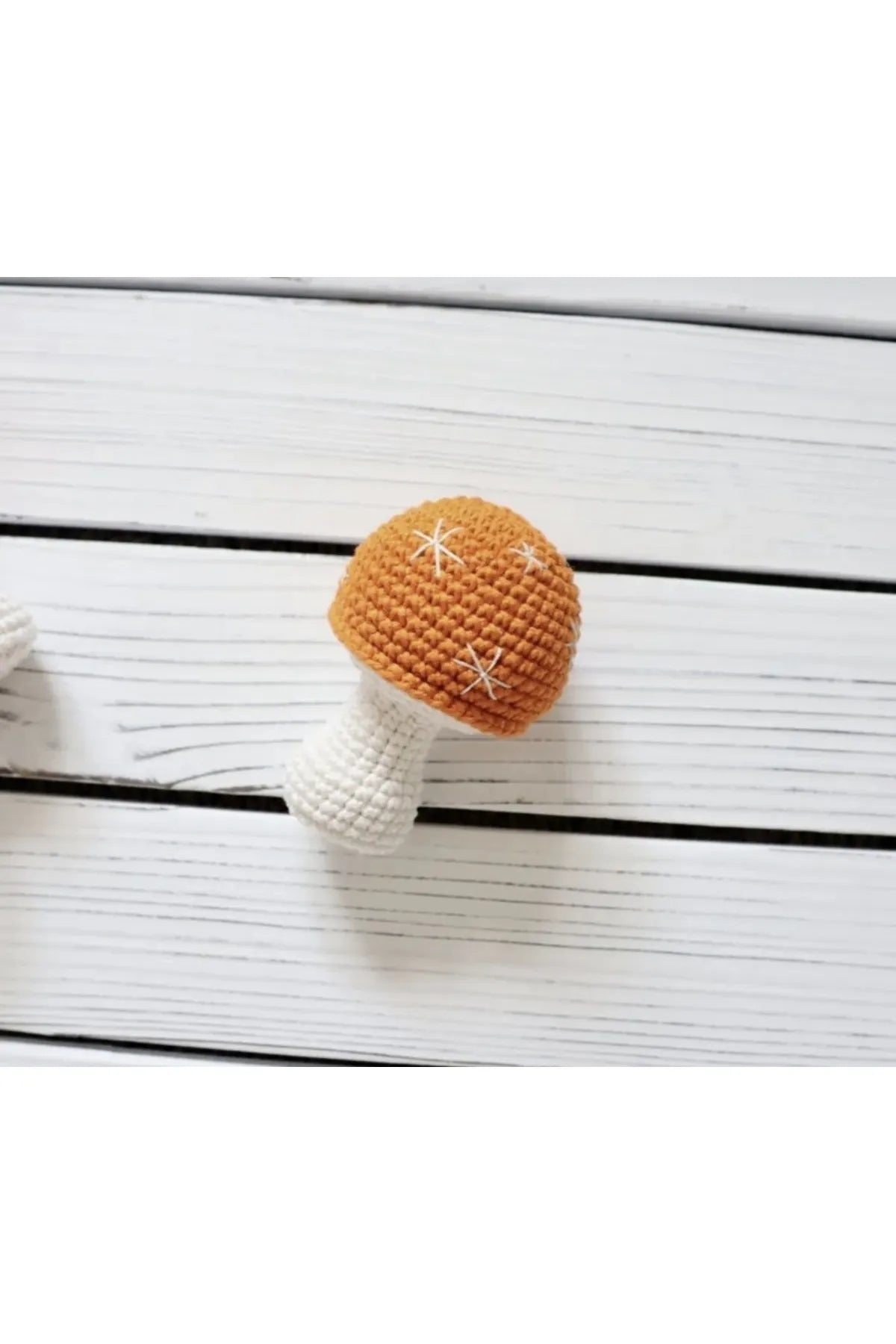Crocheted mushroom with orange cap and white stem on wooden background