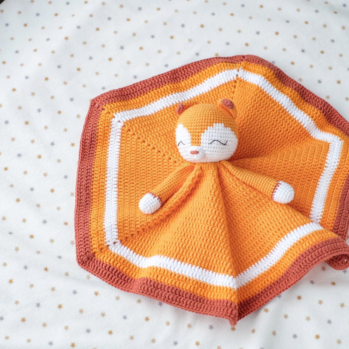 Crocheted orange and white comfort blanket with cute sleeping character on hexagonal mat