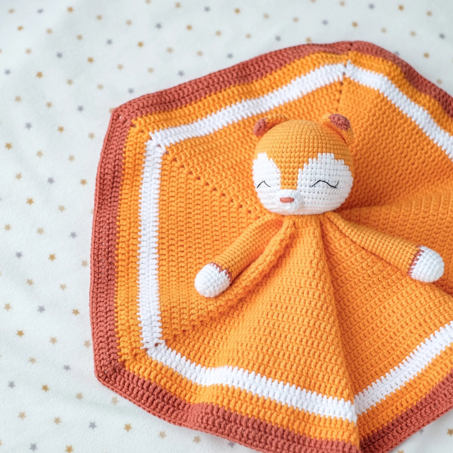 Crocheted orange and white baby lovey with smiling character on polka dot background