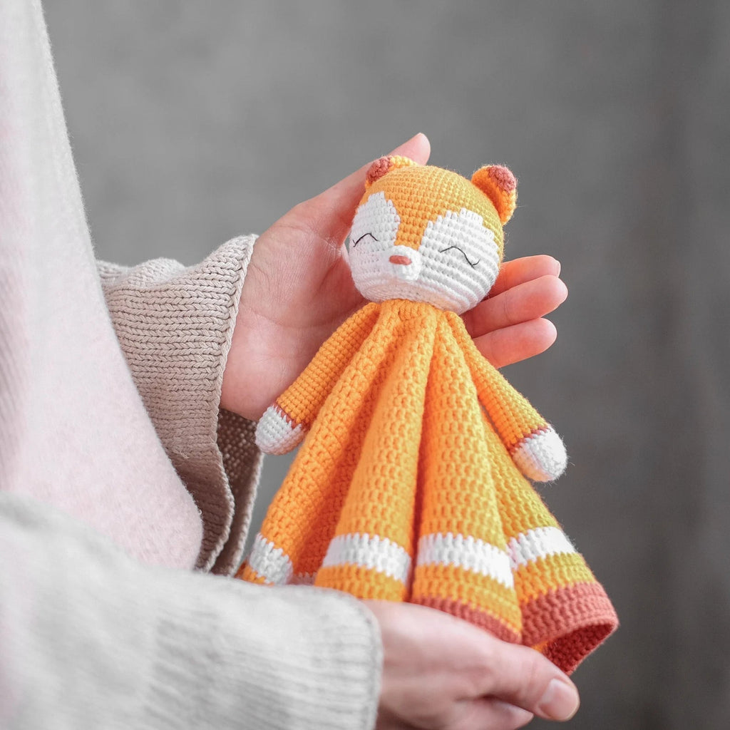Crocheted orange and white fox-like doll with closed eyes, held in a hand