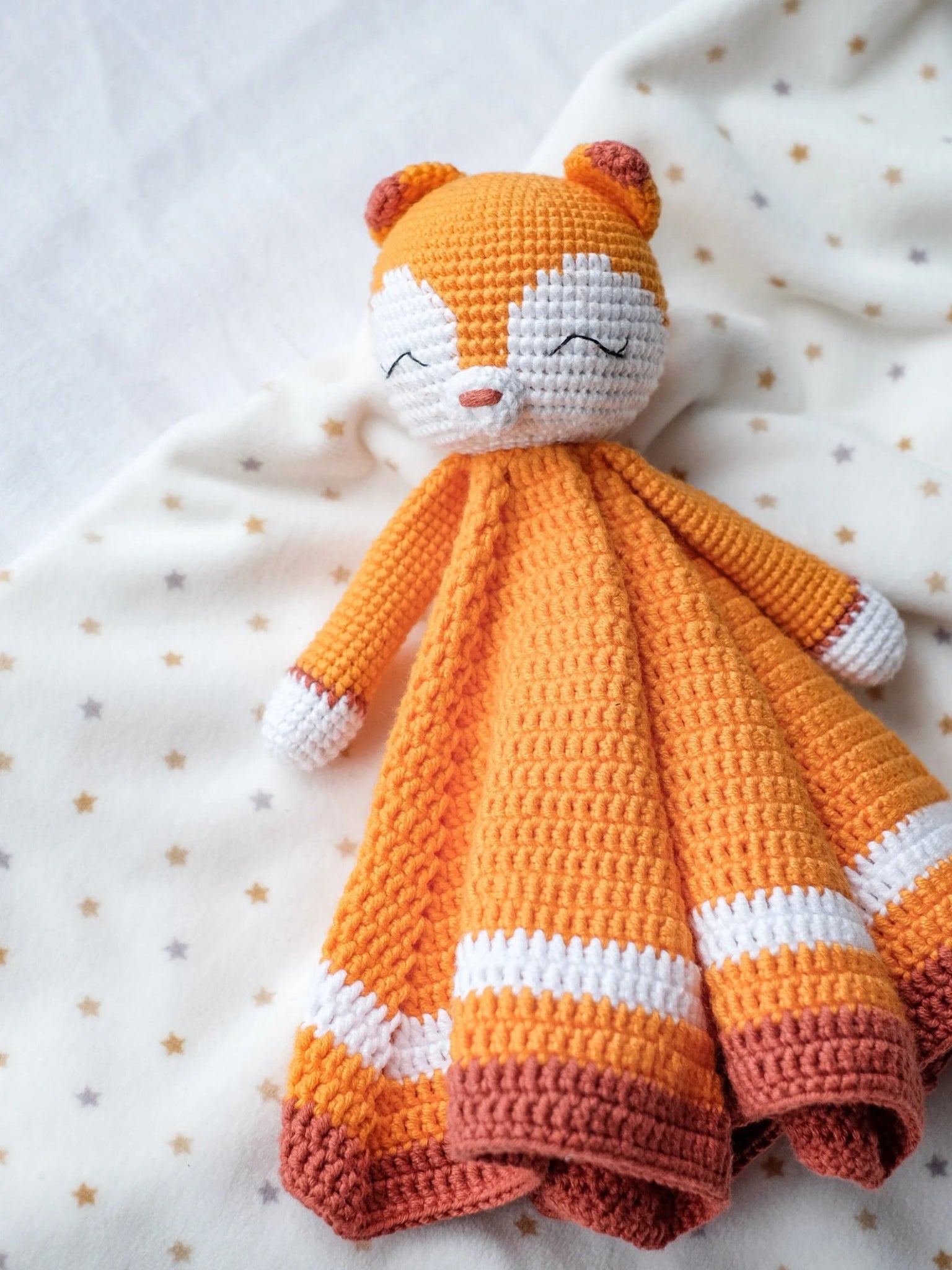Crocheted orange and white sleepy fox lovey blanket on starry background
