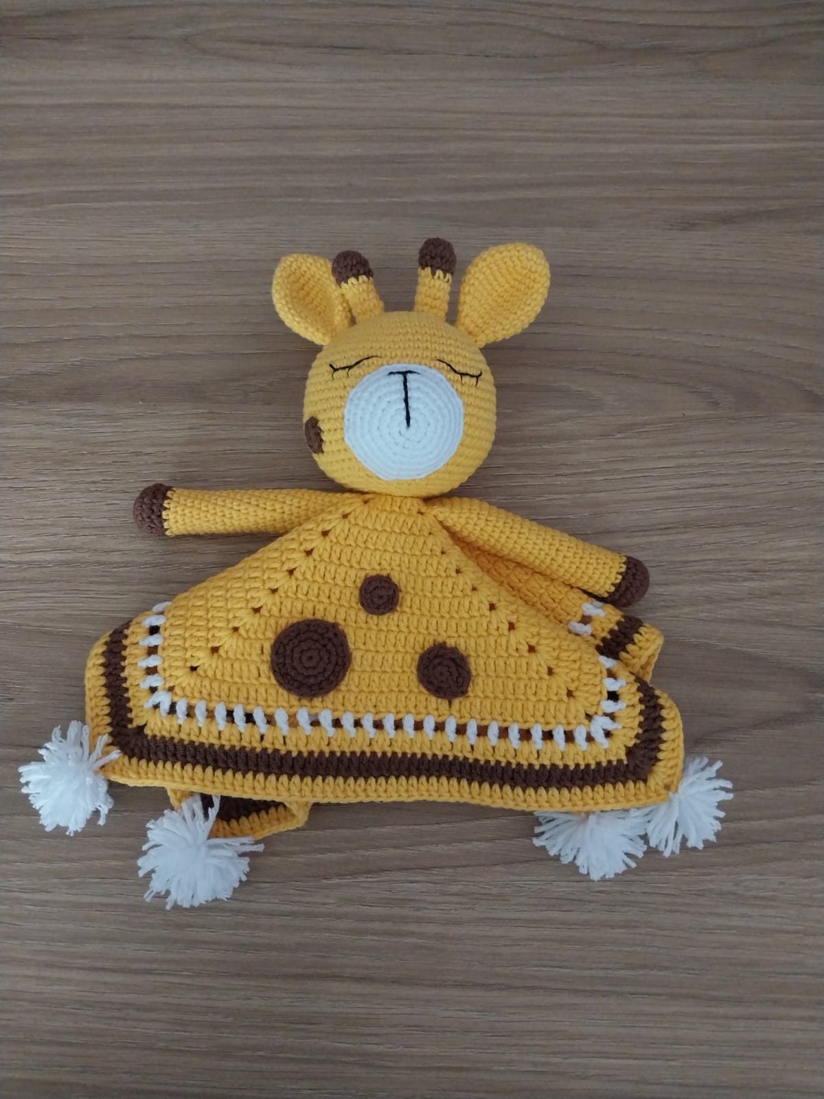 Crocheted yellow giraffe lovey blanket with brown spots and white pom-poms