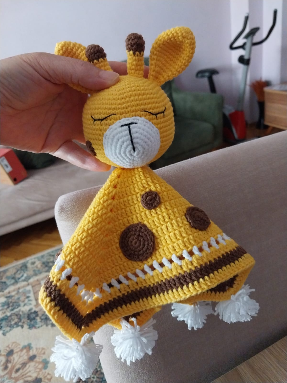 Crocheted yellow bunny lovey with brown polka dots and white pom-pom trim, held by a hand.