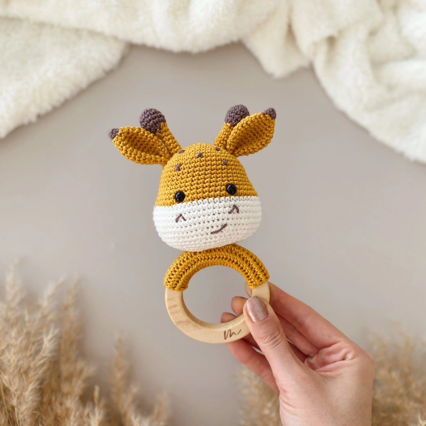 Crocheted giraffe baby teething ring with wooden base, held by hand near soft background