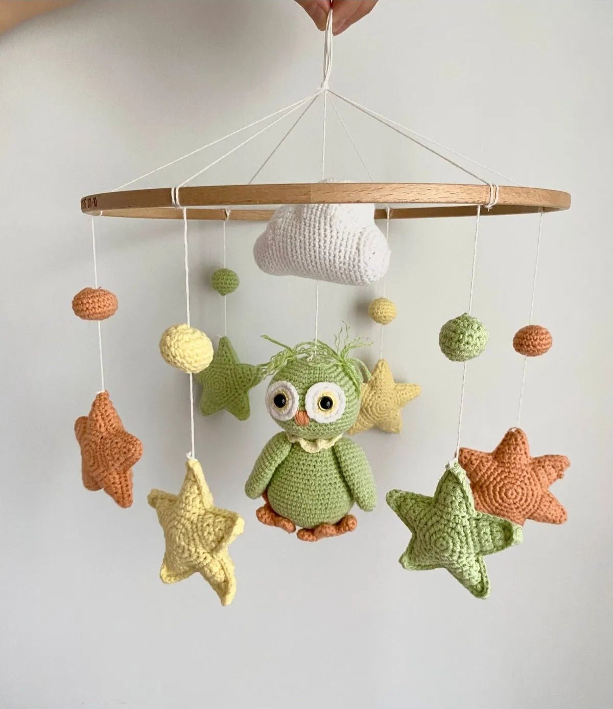 Crocheted baby mobile with green owl, stars, clouds, and colorful spheres hanging from wooden frame