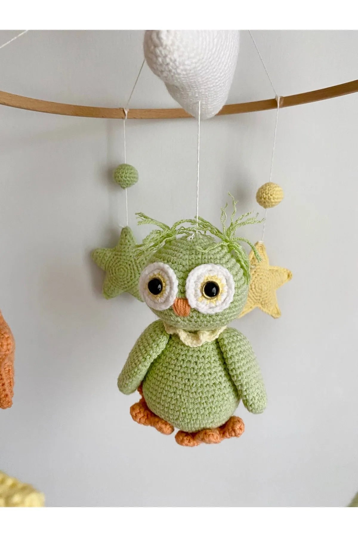 Green crocheted owl hanging from wooden mobile with yellow and white stars