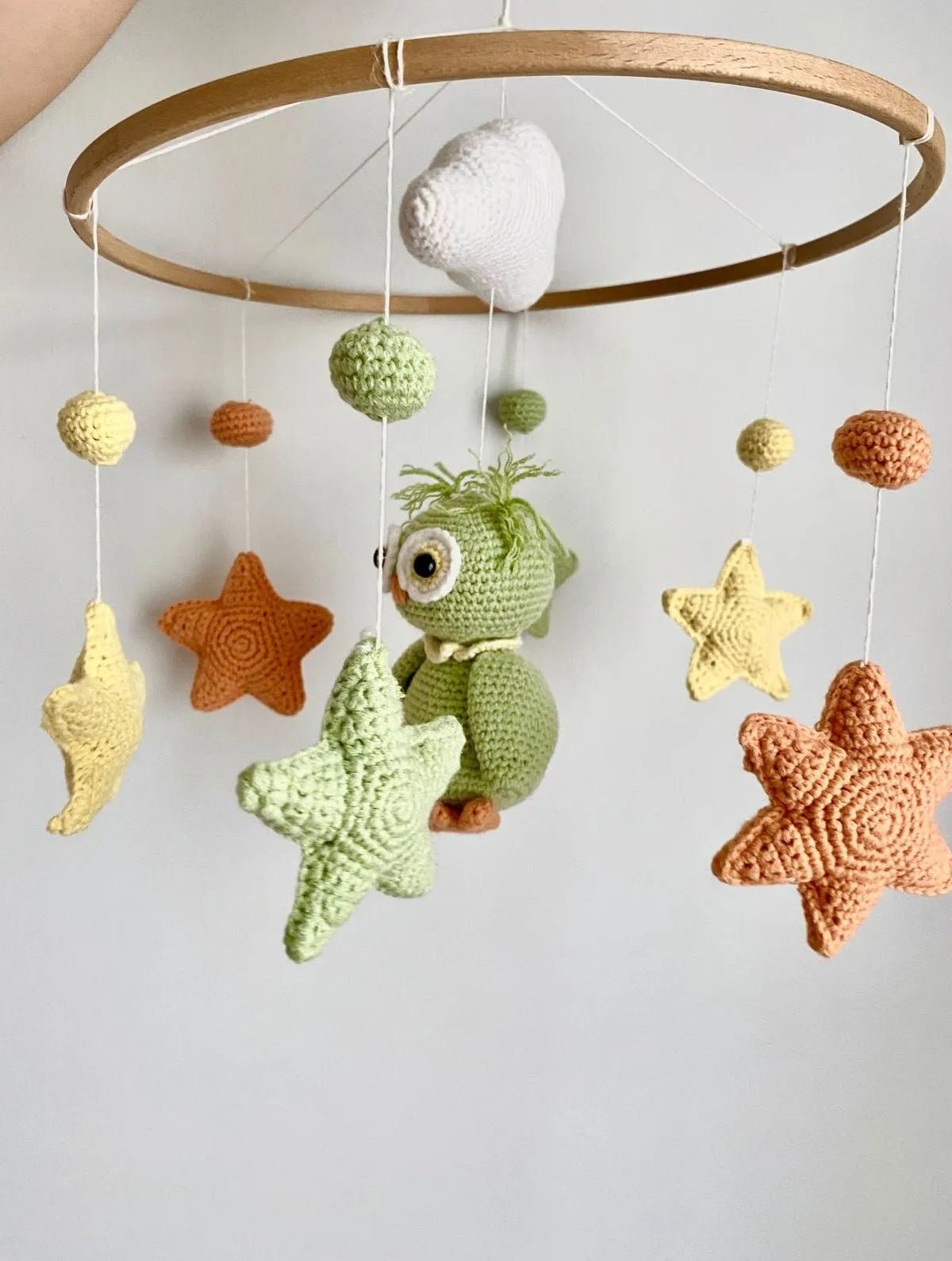 Crocheted baby mobile with green dinosaur, stars, and spheres in earth tones hanging from wooden ring