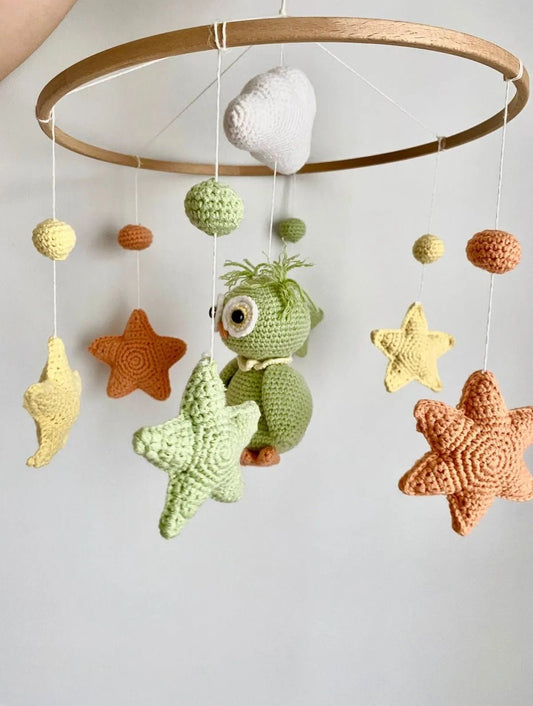 Crocheted baby mobile with green dinosaur, stars, and spheres in earth tones hanging from wooden ring