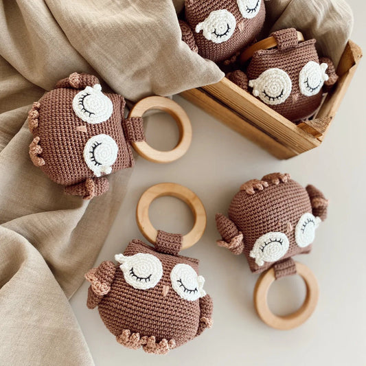 Crocheted owl-shaped baby rattles with wooden rings on neutral fabric background