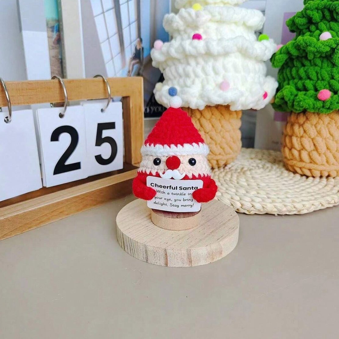 Crocheted Santa figurine with a cheerful message on wooden stand, calendar shows 25