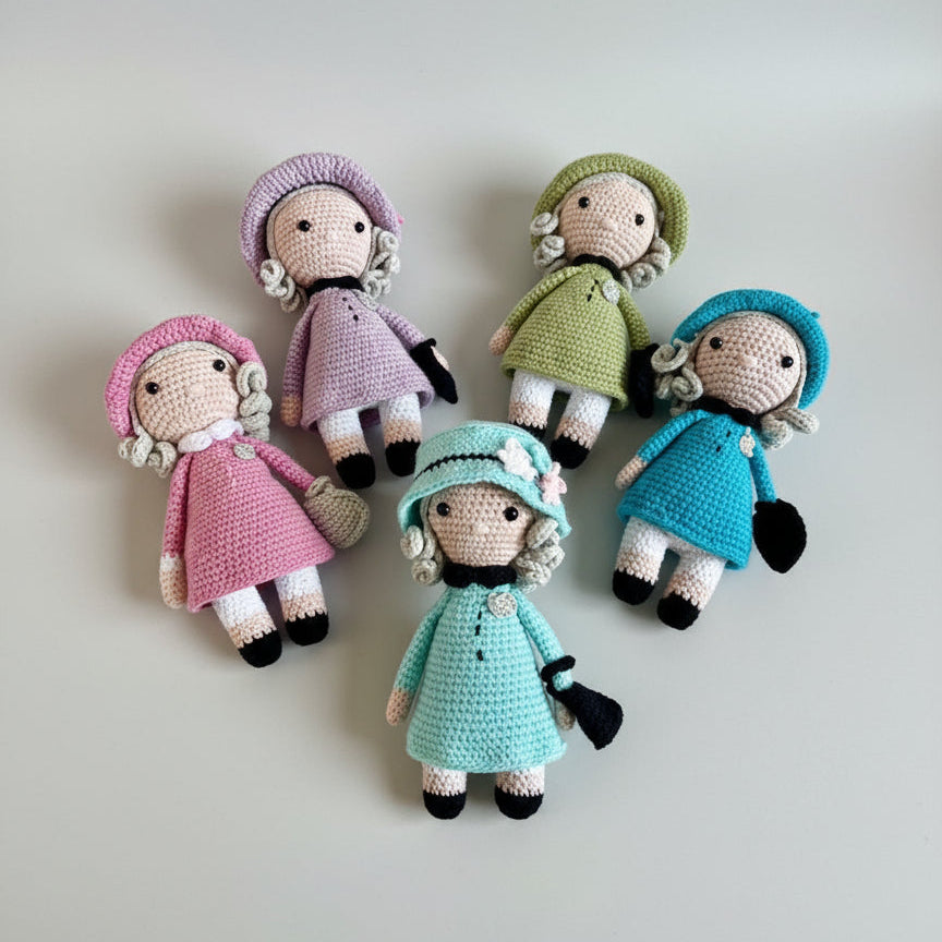 Five crocheted dolls in pastel colors with curly hair and black shoes, arranged in a circular pattern on a white background.