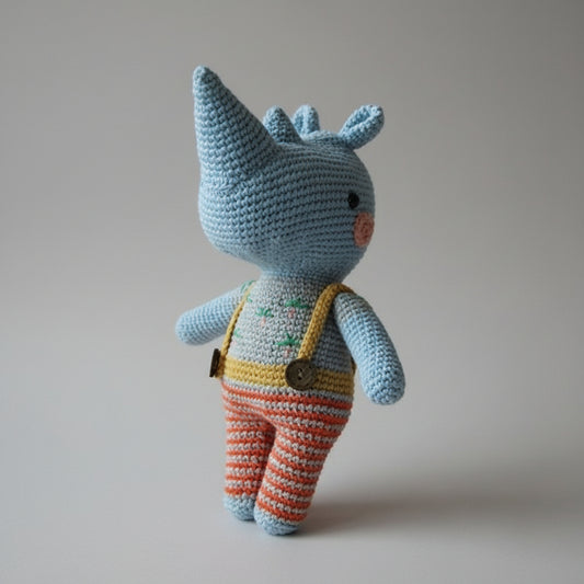 Blue crocheted rhino toy with striped overalls, standing against neutral background