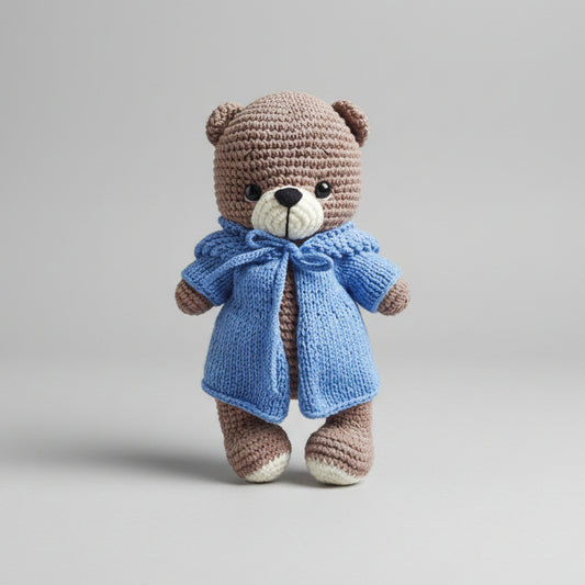 Crocheted brown teddy bear wearing a blue knitted coat and bow