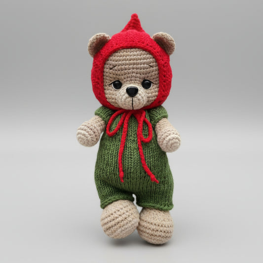 Crocheted teddy bear in red hood and green overalls with red bow tie