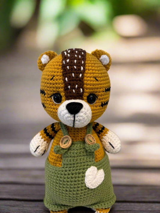 Crocheted tiger stuffed animal with green overalls and wooden button details