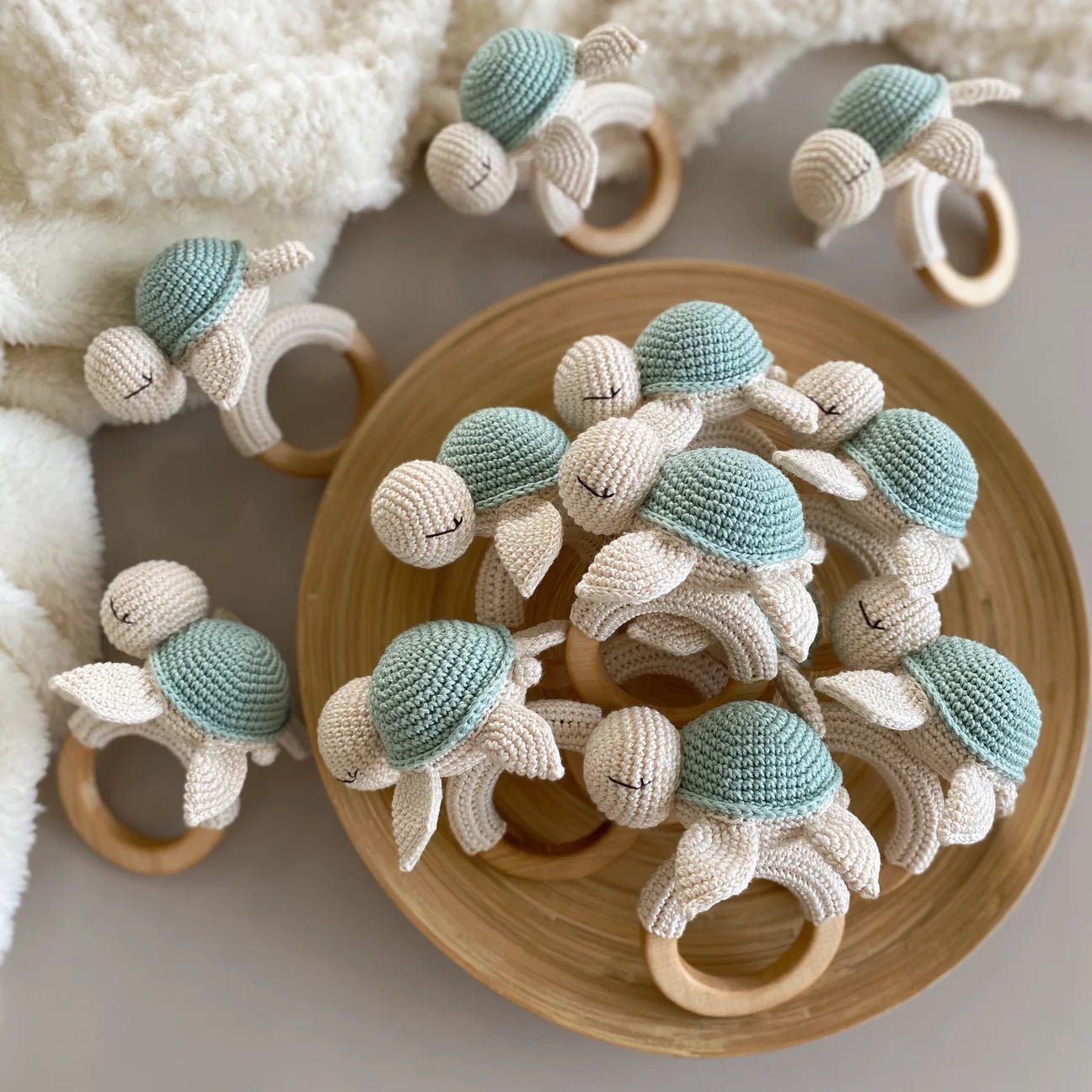 Crocheted sea turtle baby teethers in mint green and cream on wooden bowl and fluffy blanket