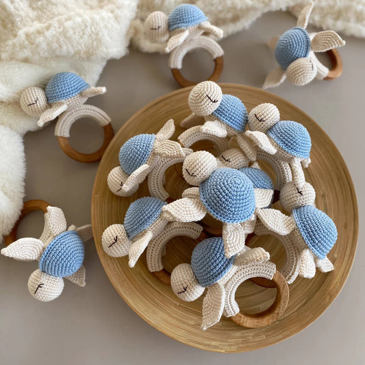 Crocheted baby rattles with blue caps and wooden rings in a wooden bowl