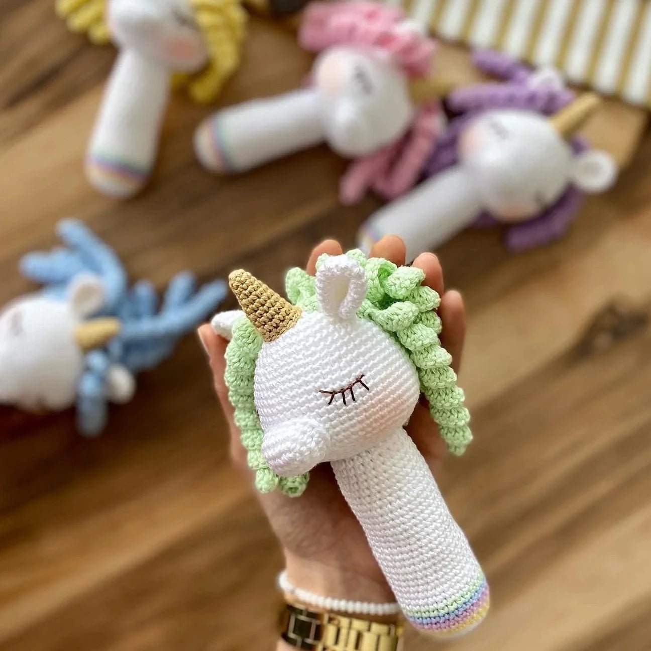 Crocheted unicorn rattle with closed eyes, white body, green mane, and golden horn
