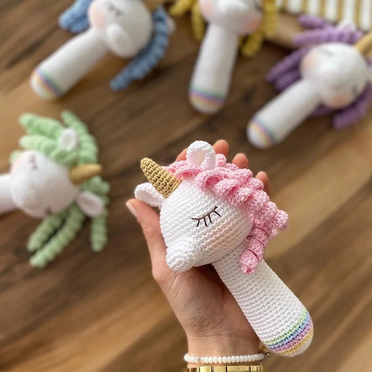 Crocheted unicorn rattle with pink mane, white body, and golden horn held in hand