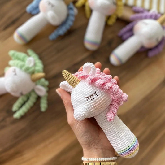 Crocheted unicorn rattle with pink mane, white body, and golden horn held in hand