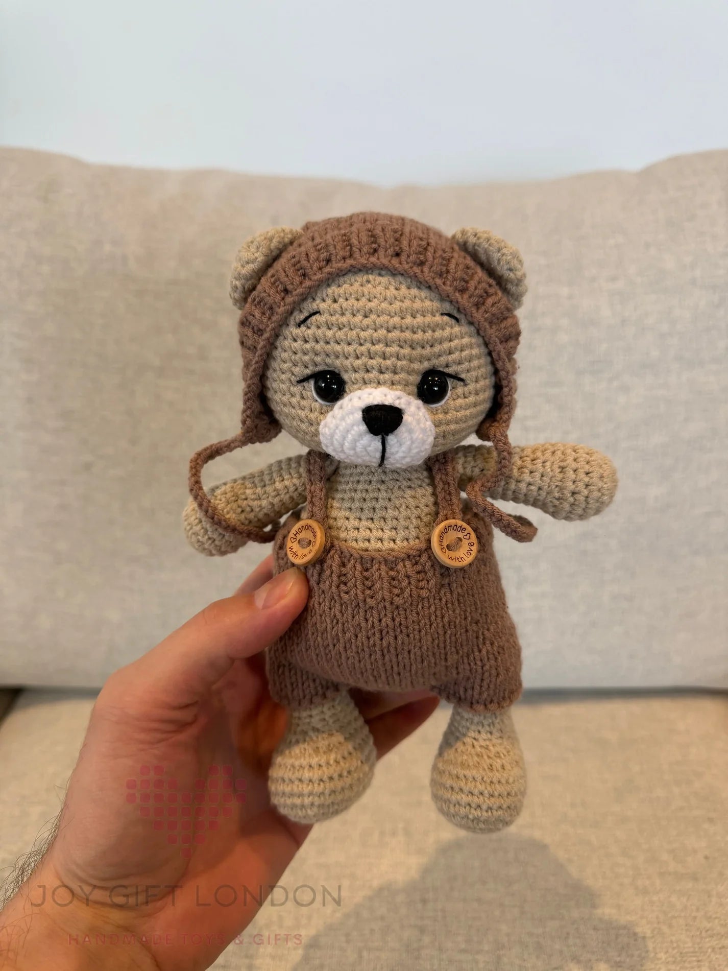 Crocheted teddy bear in brown overalls and knitted hat, held by a hand