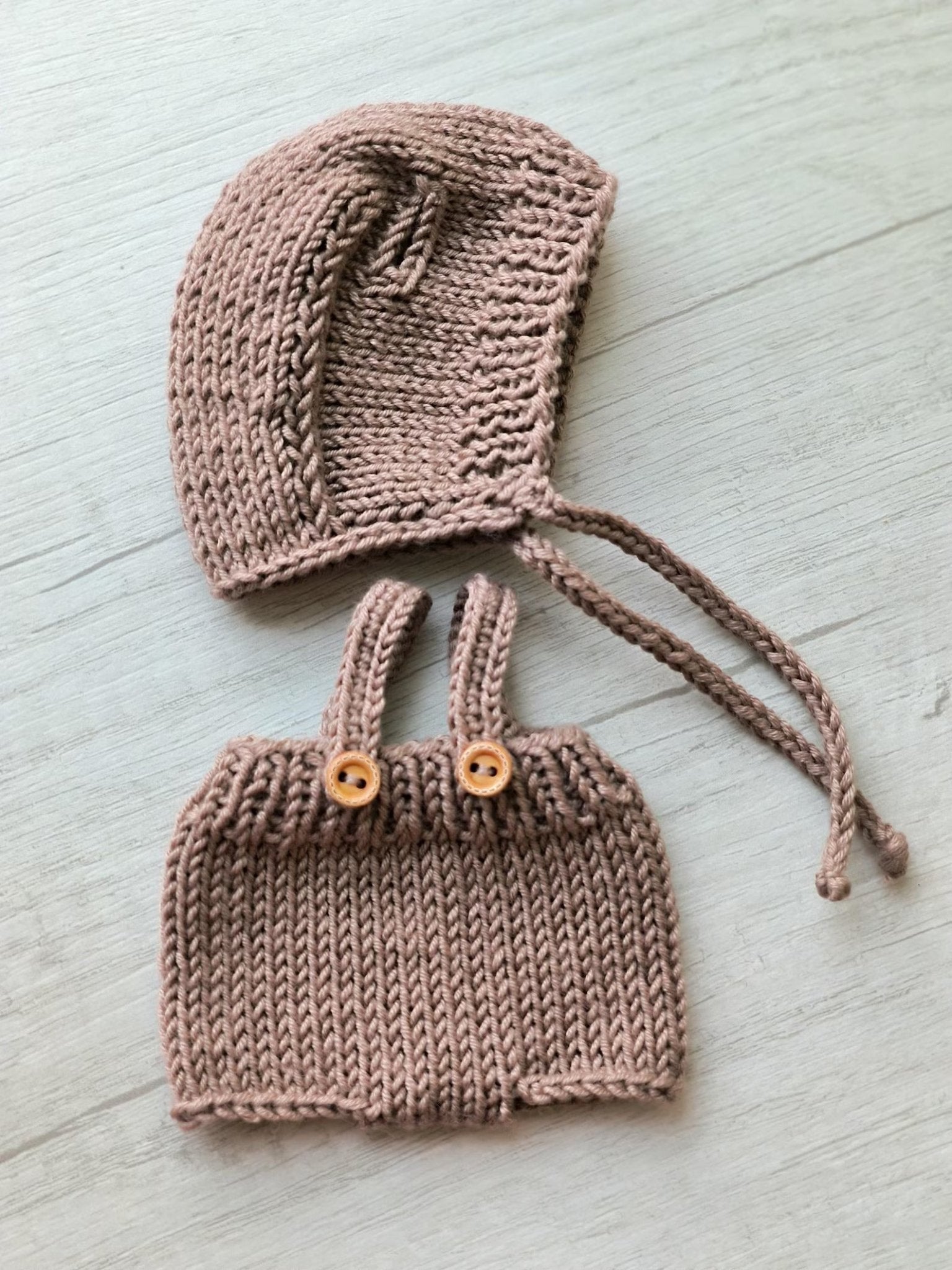 Dusty rose knitted baby bonnet and bloomers with wooden buttons on light background