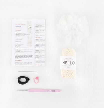 Knitting supplies including cream yarn, pattern, crochet hook, and black ring on white background