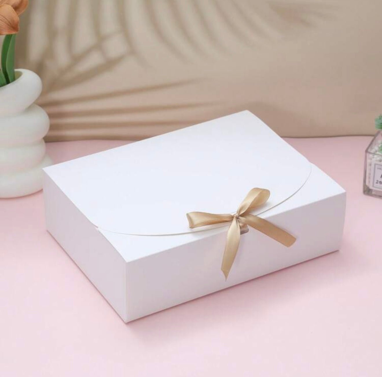 White gift box with golden ribbon on pink background, elegant and minimalist style