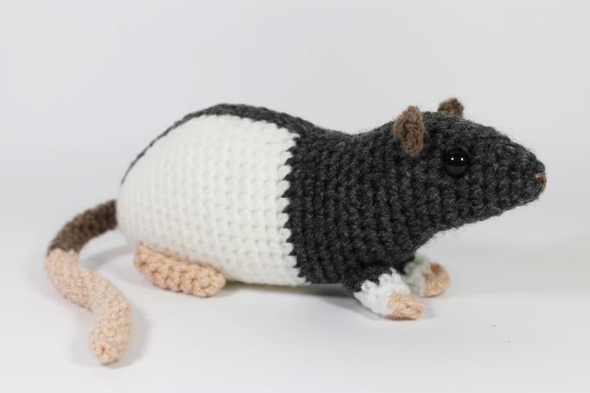 Crocheted rat with black and white body, sitting on white background