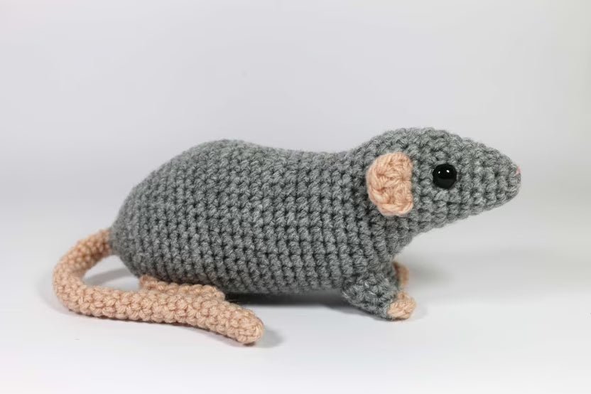 Crocheted gray mouse with peach-colored ears and tail, sitting on a white background