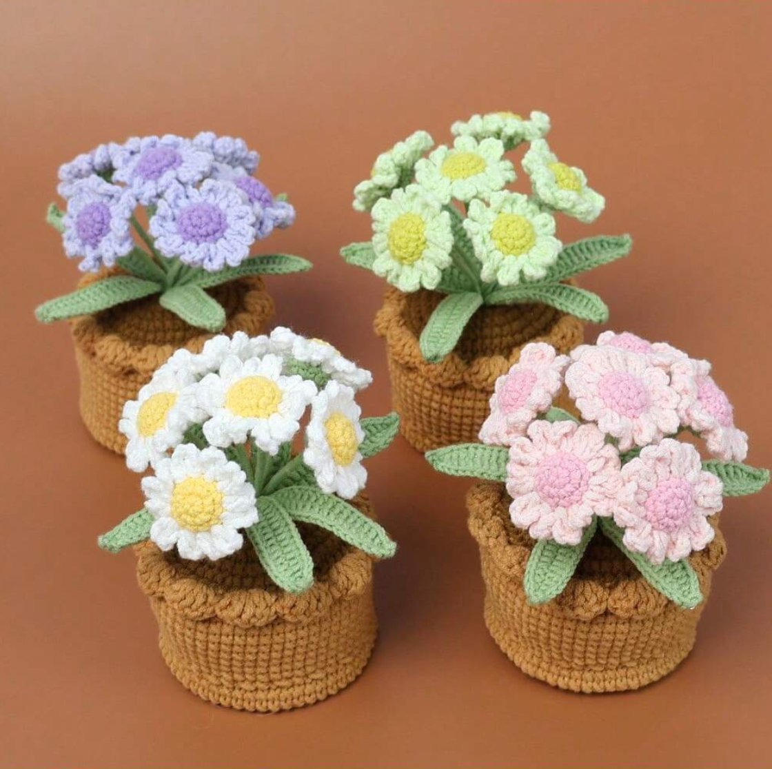 Four crocheted flower pots with colorful blooms in purple, white, green, and pink