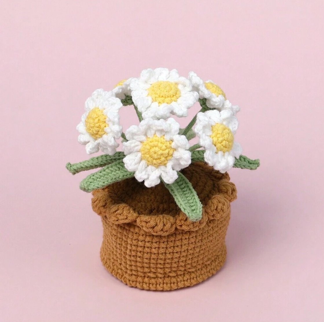 Crocheted daisies with yellow centers in a brown textured yarn basket on pink background