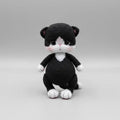 Crocheted black and white cat plush toy sitting on a plain background