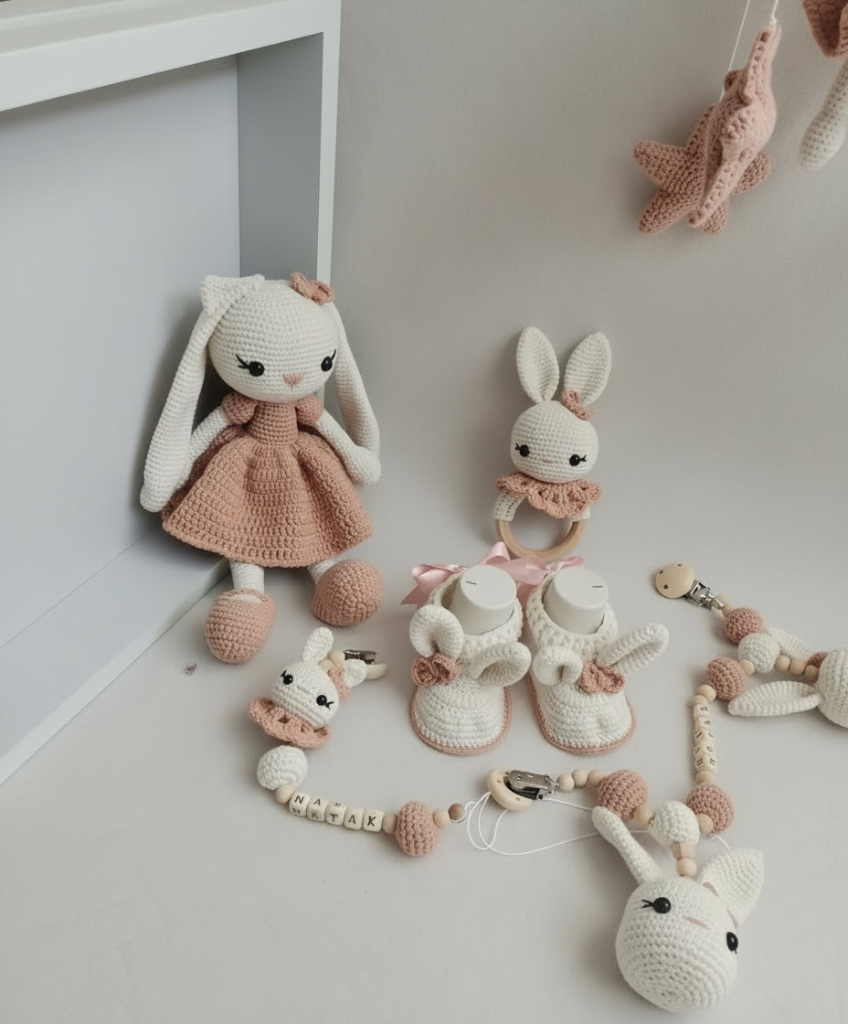 Handmade crochet bunny dolls, booties, and accessories in soft pink and white tones.