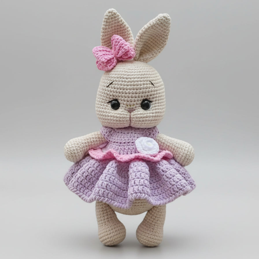 Crocheted bunny with pink bow and lavender dress, standing against neutral background