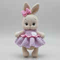 Crocheted bunny with pink bow and lavender dress, standing against neutral background