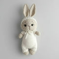 Crocheted bunny in white outfit with long ears, sitting against gray background