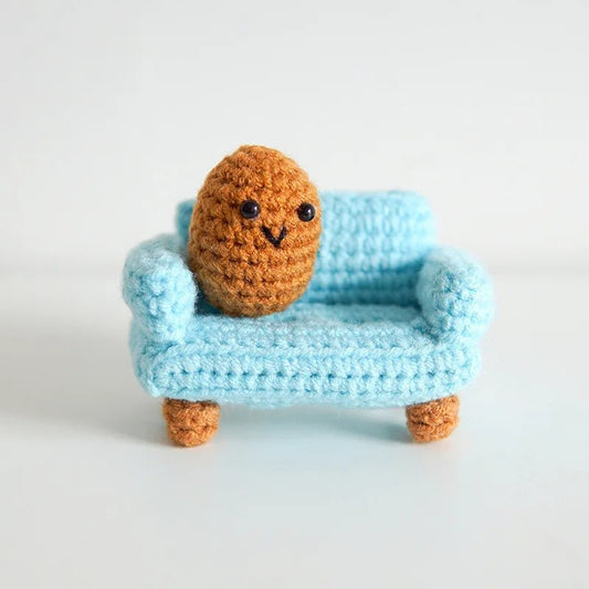 Crocheted orange potato character sitting on a blue knitted couch with tiny legs