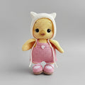 Crocheted yellow chick in pink overalls and white cat-ear hat on gray background