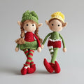 Two crocheted elf dolls in Christmas colors, with pom-pom hats and striped stockings, holding hands.